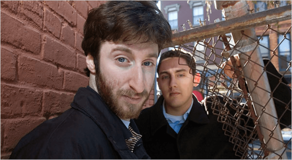 Sur la photo, on voit Holden Karfnosky et un jeune homme devant un mur de briques rouges ; l'un est au premier plan et regarde directement vers l'appareil photo, tandis que l'autre est derrière, légèrement flou.