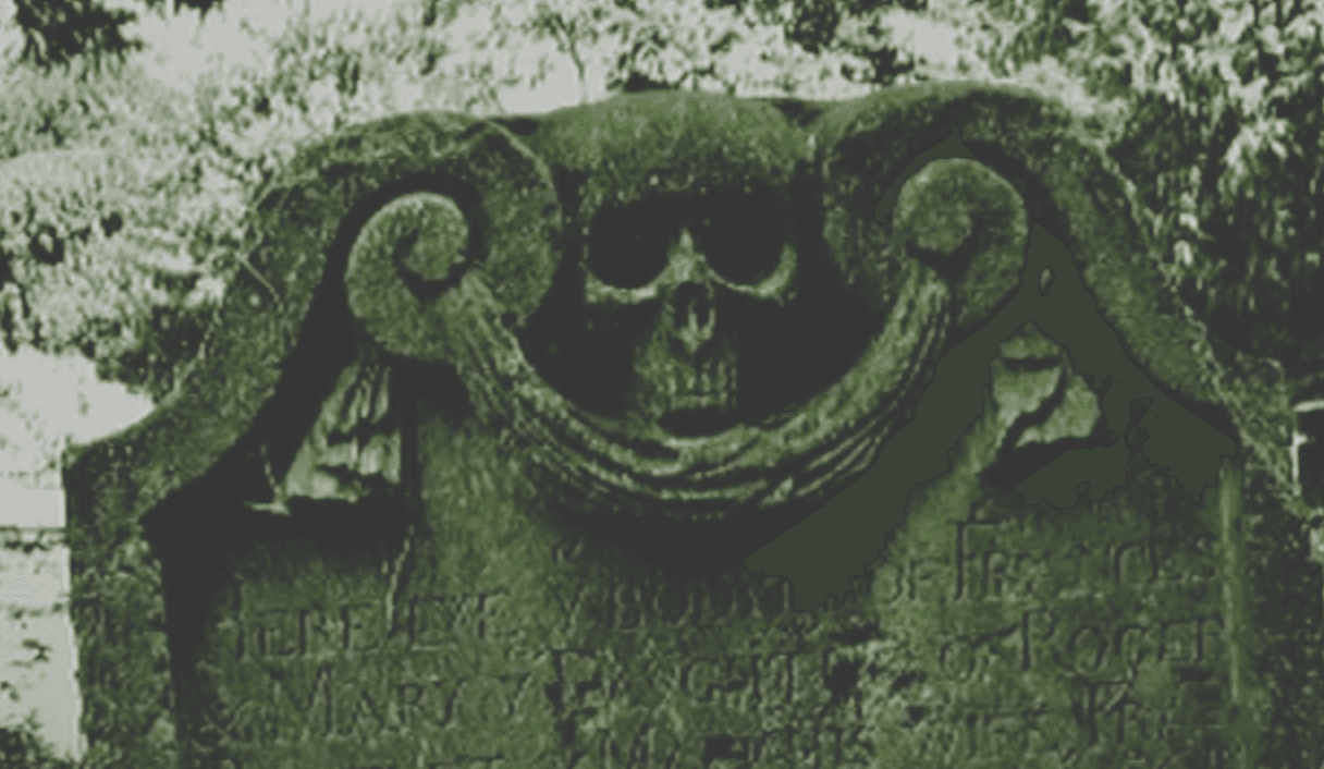 L'image montre une vieille pierre tombale usée avec un crâne sculpté dessus et un texte qu'on ne peut pas lire à cause de l'usure.