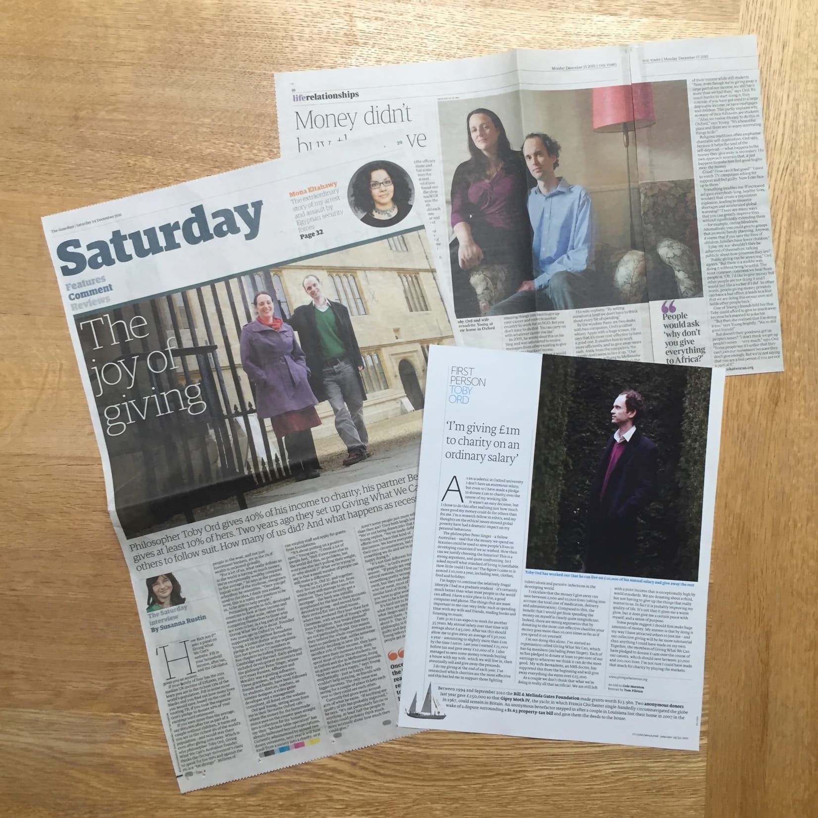 L'image montre plusieurs pages d'un journal étalées sur une surface en bois, avec des articles sur les organismes de bienfaisance.