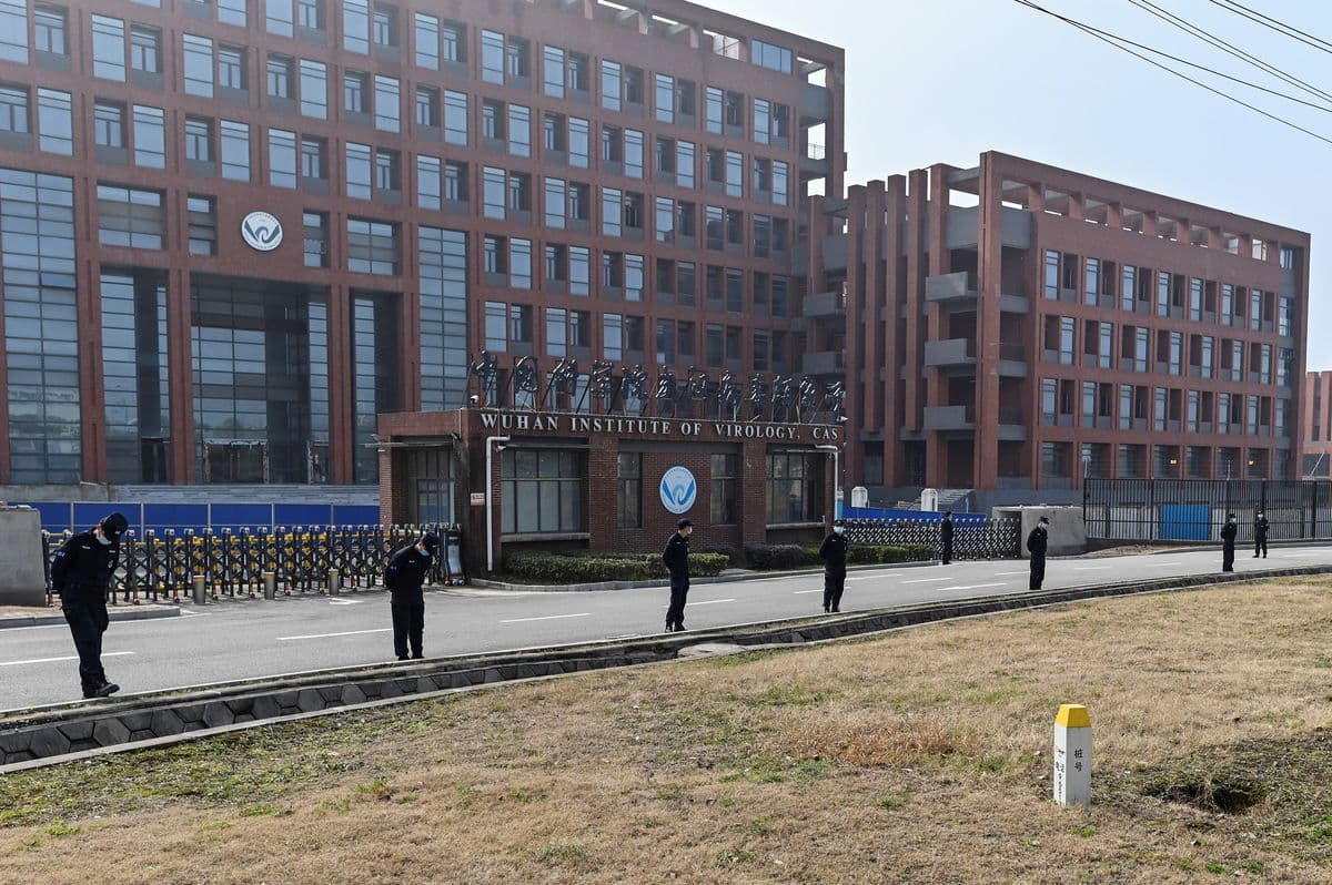 L'image montre la façade de l'« Institut de virologie de Wuhan », avec des gardes de sécurité patrouillant devant le bâtiment.