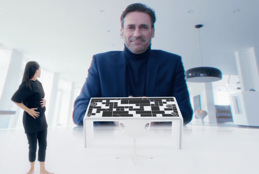 L'image montre une femme debout devant un grand écran, avec un homme souriant et se penchant vers elle. Devant la femme se trouve une table de contrôle de style futuriste.