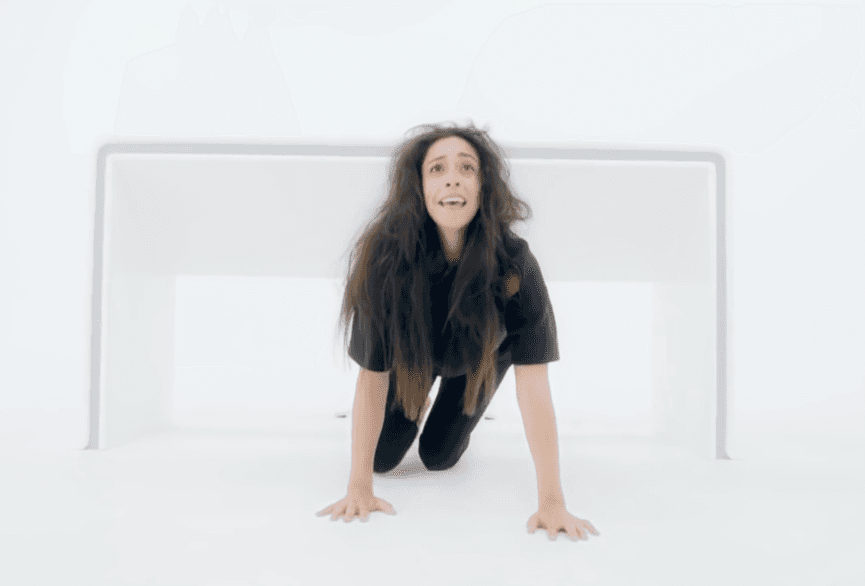 L'image montre une femme agenouillée avec les mains sur le sol dans une pièce blanche, son expression indiquant la peur et la souffrance.